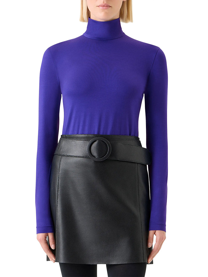 A person wearing an Akris Punto Mock Neck Signature Dot Jersey Turtleneck in Ultra Violet paired with a black belted skirt.