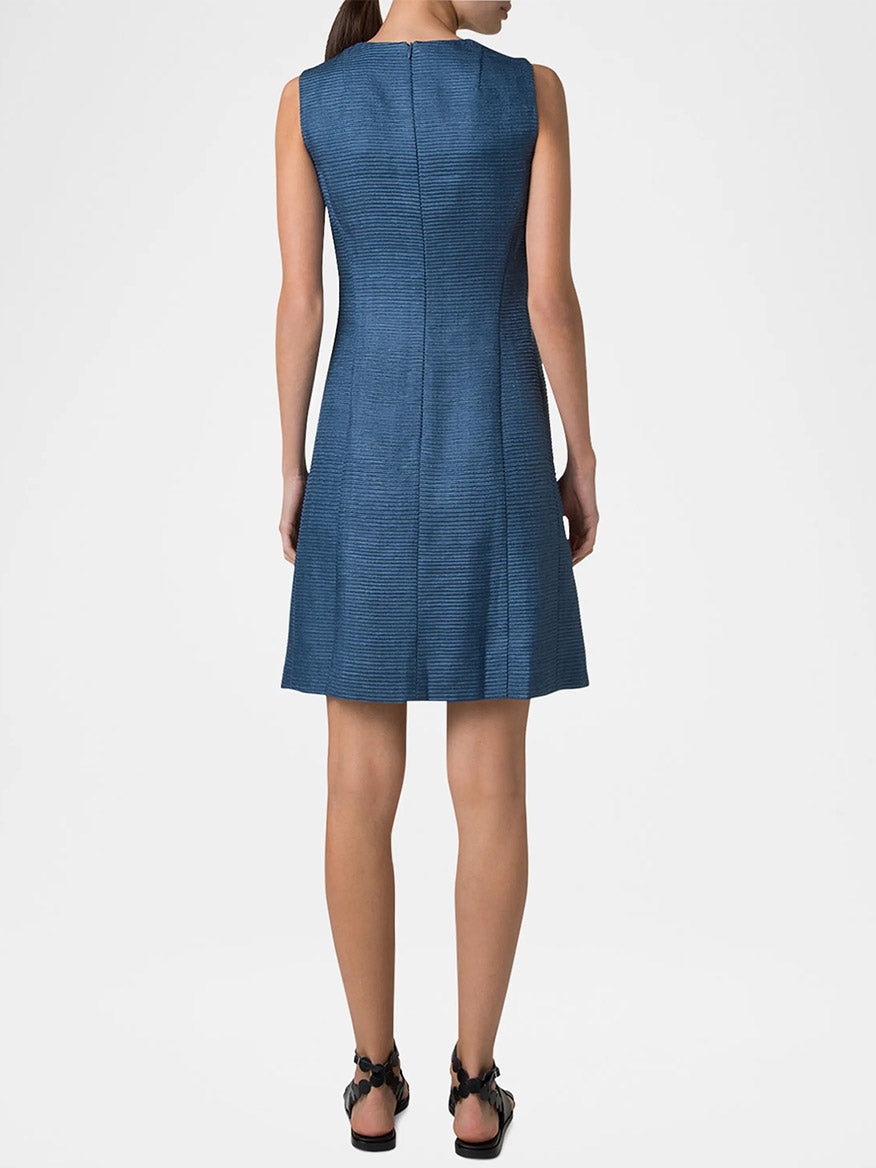 A woman elegantly dons the Akris Punto Sleeveless Silk Ottoman Shift Dress in Medium Blue, highlighting its textured design from behind. Her look is polished off with stylish black sandals for a touch of simple sophistication.