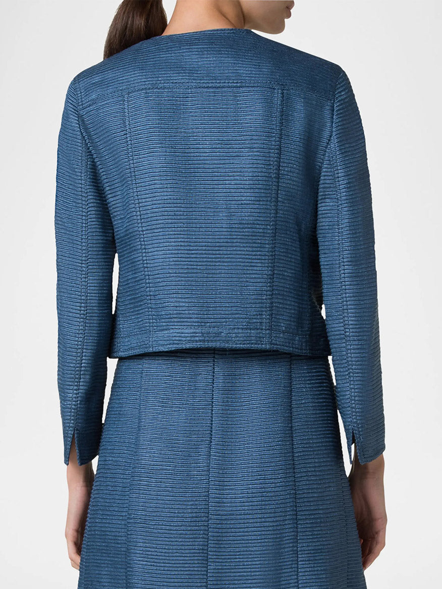 A rear view of a person in the Akris Punto Cropped Silk Ottoman Jacket in medium blue and matching skirt, with a round neckline, standing against a neutral background.