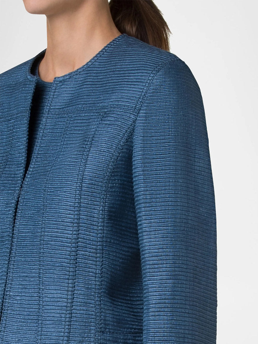 Someone is wearing the Akris Punto Cropped Silk Ottoman Jacket in Medium Blue, featuring a textured design and round neckline, with their hair tied back.