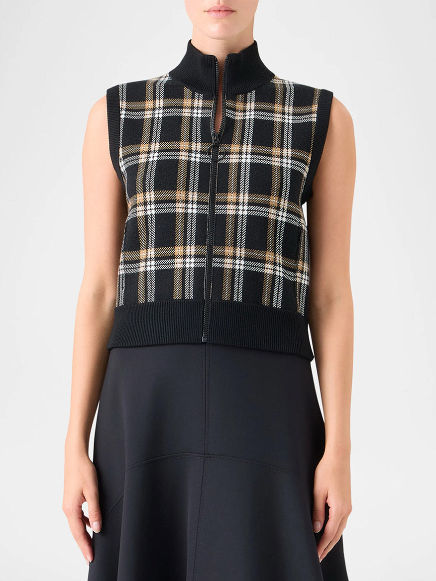 A person models the Akris Punto Sleeveless Plaid Jacquard Zip Sweater in Black/Cream/Camel over a black skirt or dress, shown from shoulders to mid-thigh.