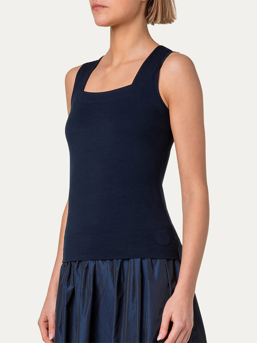 A person wearing an Akris Punto Square-Neck Jersey Tank Top in Ink and a pleated navy blue skirt is shown facing slightly to the side against a plain background.