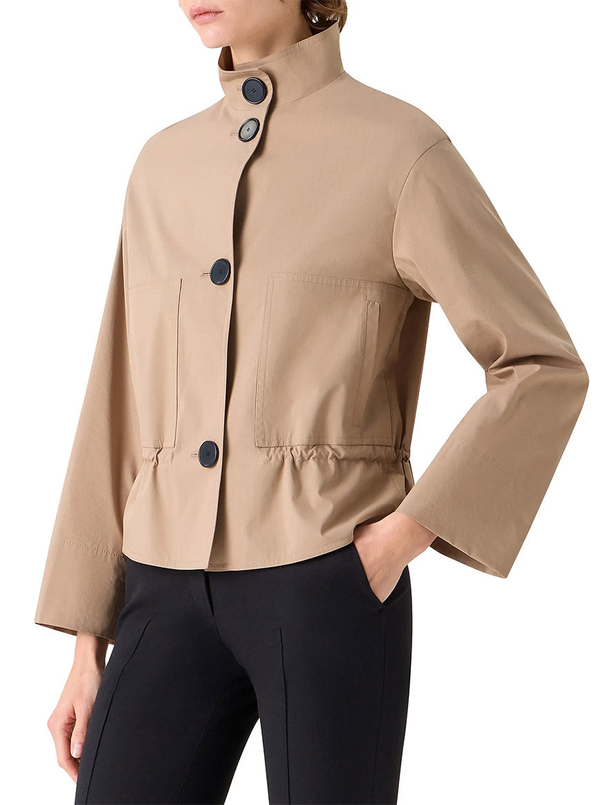 A person wearing the Akris Punto Stand Collar Parka in beige, featuring large black buttons, front pockets, and an adjustable drawstring waist, styled with black pants.