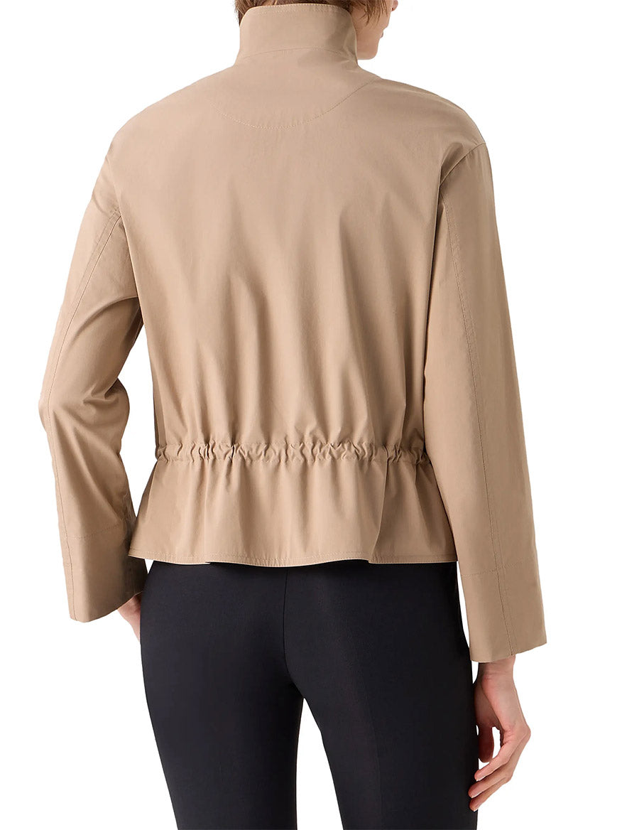 A person shown from the back wears the Akris Punto Stand Collar Parka in Beige, a long-sleeve jacket with an adjustable drawstring waist, paired with black leggings.