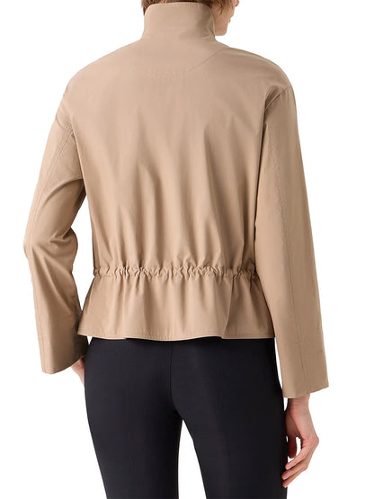 A person shown from the back wears the Akris Punto Stand Collar Parka in Beige, a long-sleeve jacket with an adjustable drawstring waist, paired with black leggings.