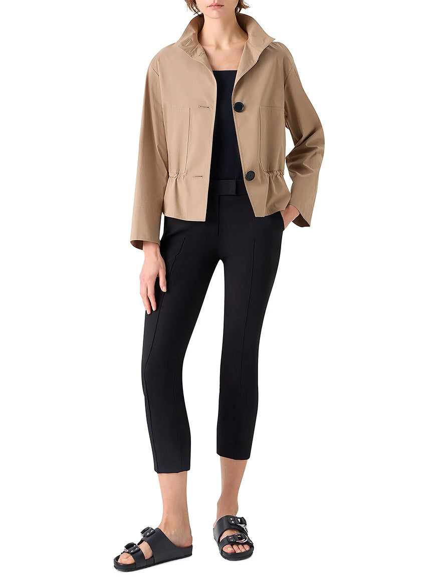A person wears the Akris Punto Stand Collar Parka in Beige over a black top and cropped pants with black slide sandals, standing against a white background.