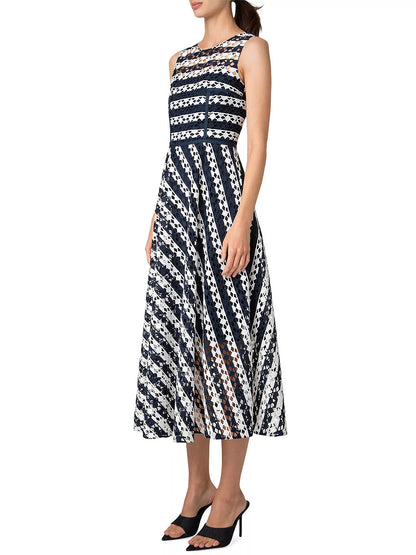 A woman is elegantly dressed in an Akris Punto Striped Dot Guipure Lace Maxi Dress in navy and cream, perfectly paired with black high-heeled mules.