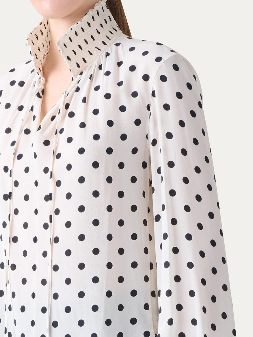 A person wearing the Akris Punto Smocked Polka Dot Silk Blouse in cream and black, featuring a high, pleated collar.