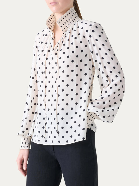 A person wearing the Akris Punto Smocked Polka Dot Silk Blouse in Cream/Black with black trousers, standing against a plain background.