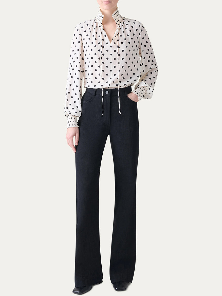 A person wearing the Akris Punto Smocked Polka Dot Silk Blouse in Cream/Black with high-waisted black flared pants, standing against a plain light background.
