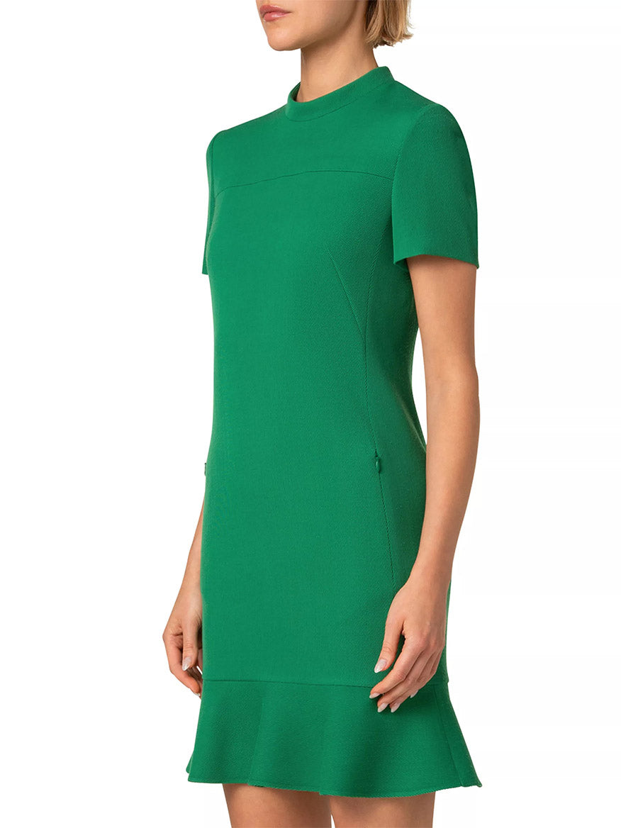 A person in a sea green, short-sleeved Akris Punto Stand Collar Ruffled Hem Tricotine Dress poses gracefully against a white background.