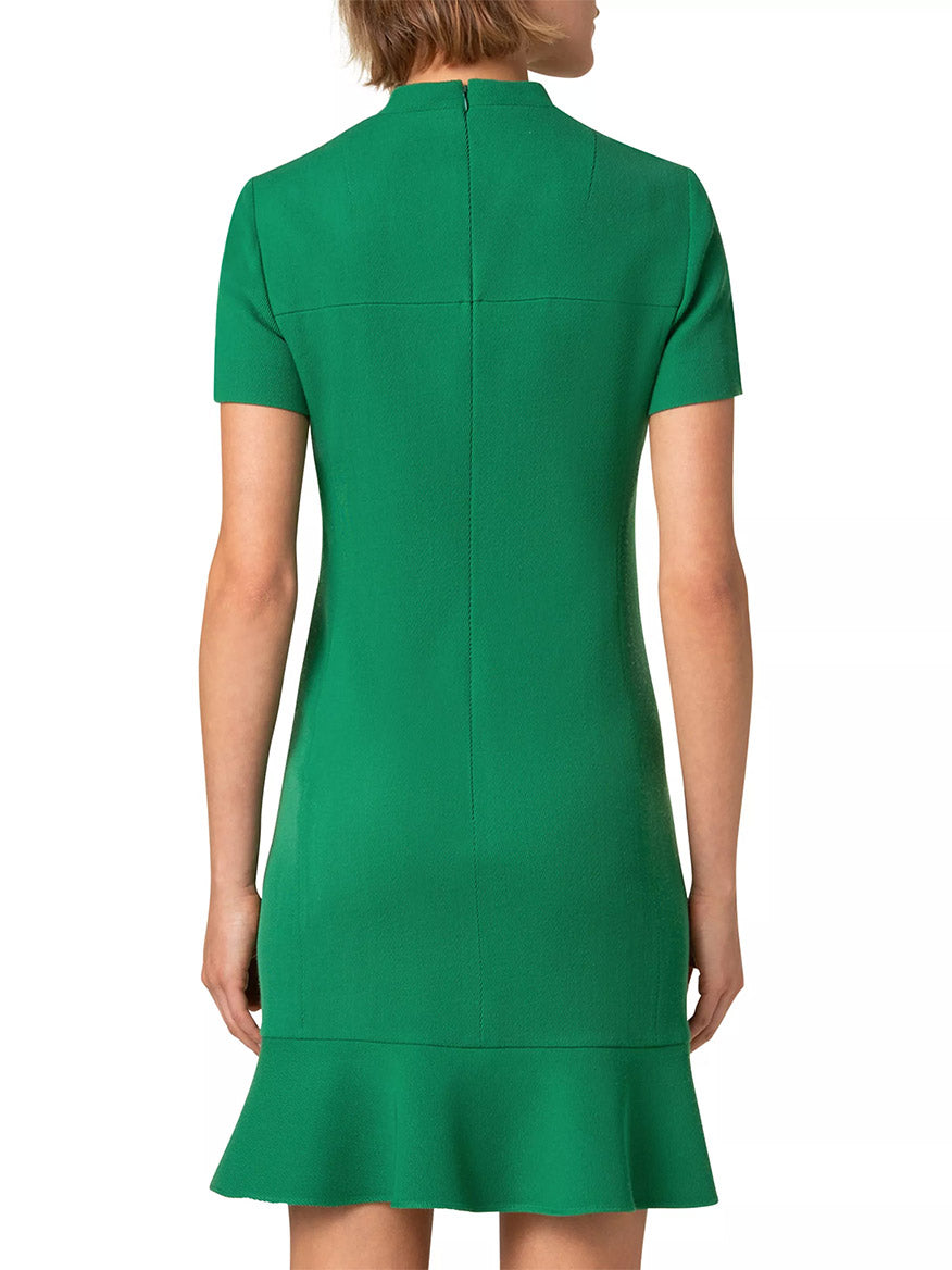 The woman stands gracefully in an Akris Punto Stand Collar Ruffled Hem Tricotine Dress in Sea Green, highlighting its elegant hue and subtle zipper back, while the ruffled hem adds a playful touch as she faces away from the camera.