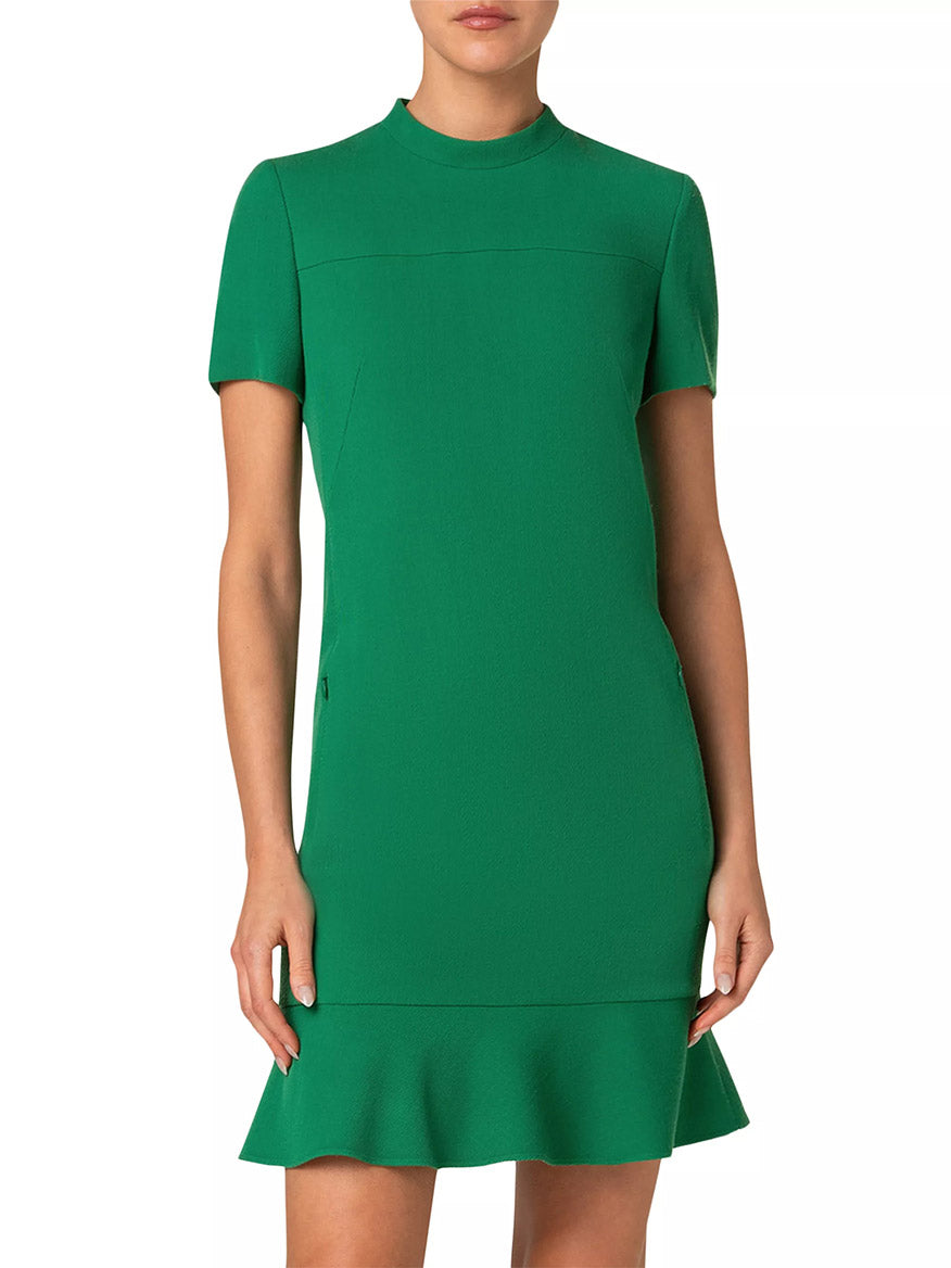 A person elegantly stands against a plain white backdrop, wearing an Akris Punto Stand Collar Ruffled Hem Tricotine Dress in Sea Green with short sleeves.