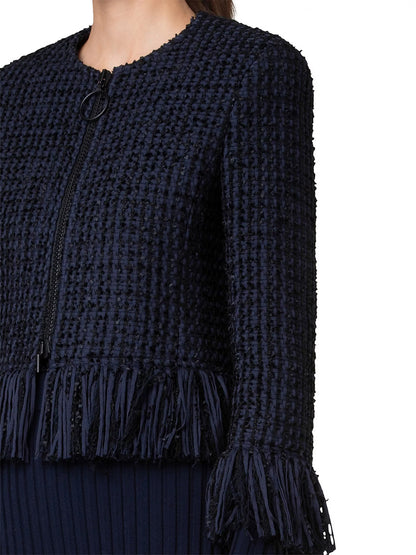 A close-up of a person wearing the Akris Punto Chunky Tweed Cropped Jacket With Fringe in Navy, featuring intricate fringe detailing at the hem and ends of the sleeves. The jacket is designed with a circular clasp closure near the top.