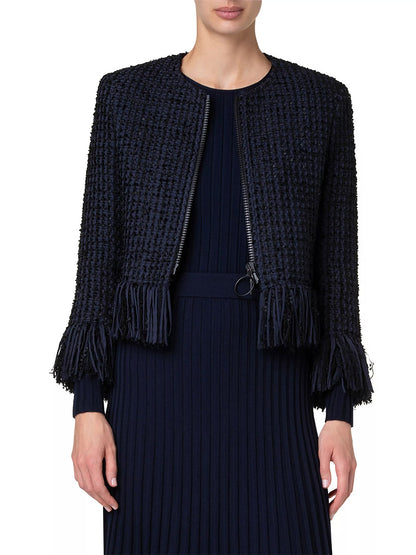 A person wearing an Akris Punto chunky tweed cropped jacket with fringe in navy over a long pleated black dress.