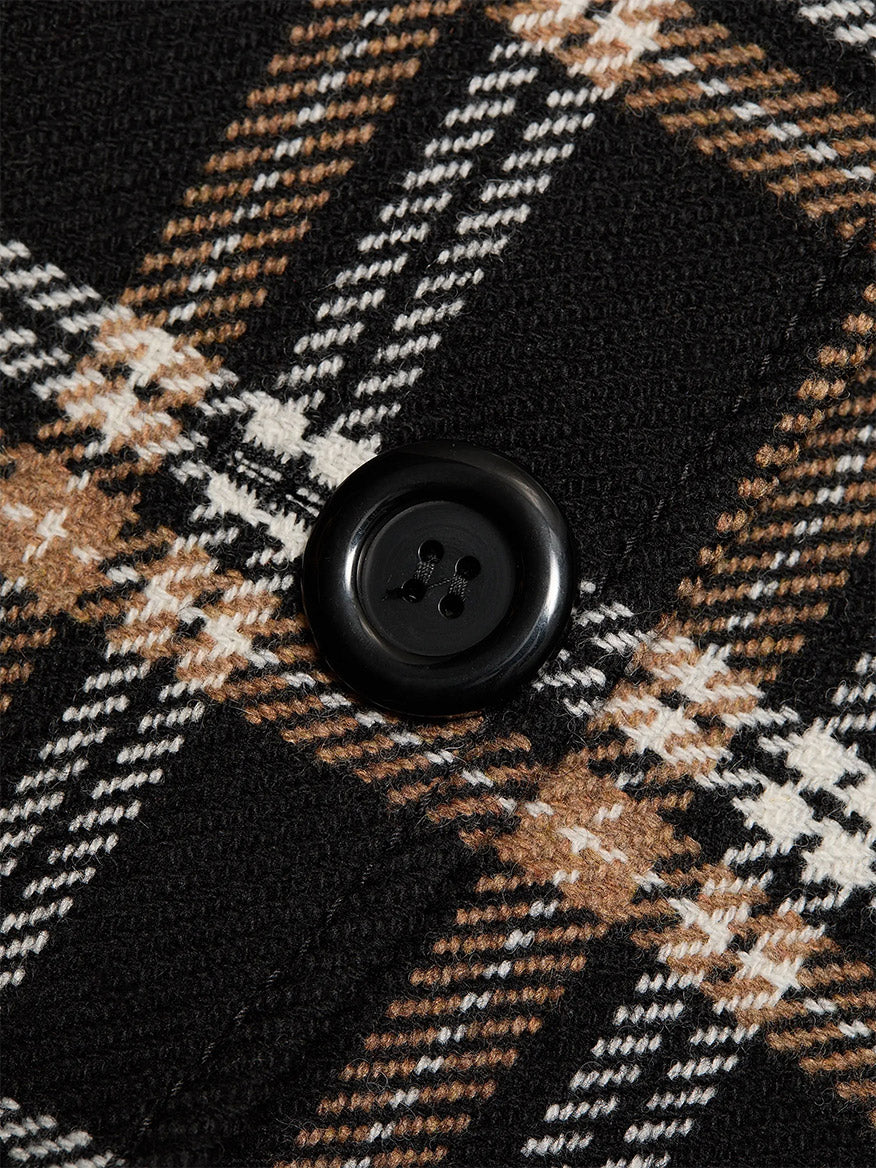 Close-up of a black button on the Akris Punto Tweed Plaid Structured Blazer in Black/Camel/Cream, featuring black, white, and brown plaid fabric.