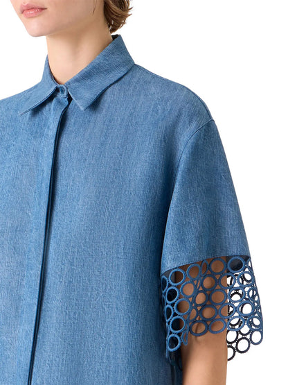 Someone wears the Akris Punto Washed Denim Circle Lace Shirt in medium blue, featuring a boxy fit, pointed collar, and open-circle lace detail on the elbow-length sleeves.