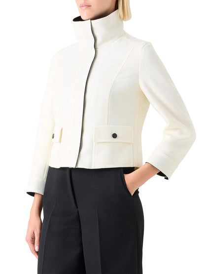 A person wears the Akris Punto Wool Tricotine Stand Collar Jacket in Cream/Black with black high-waisted pants, standing with one hand in their pocket.