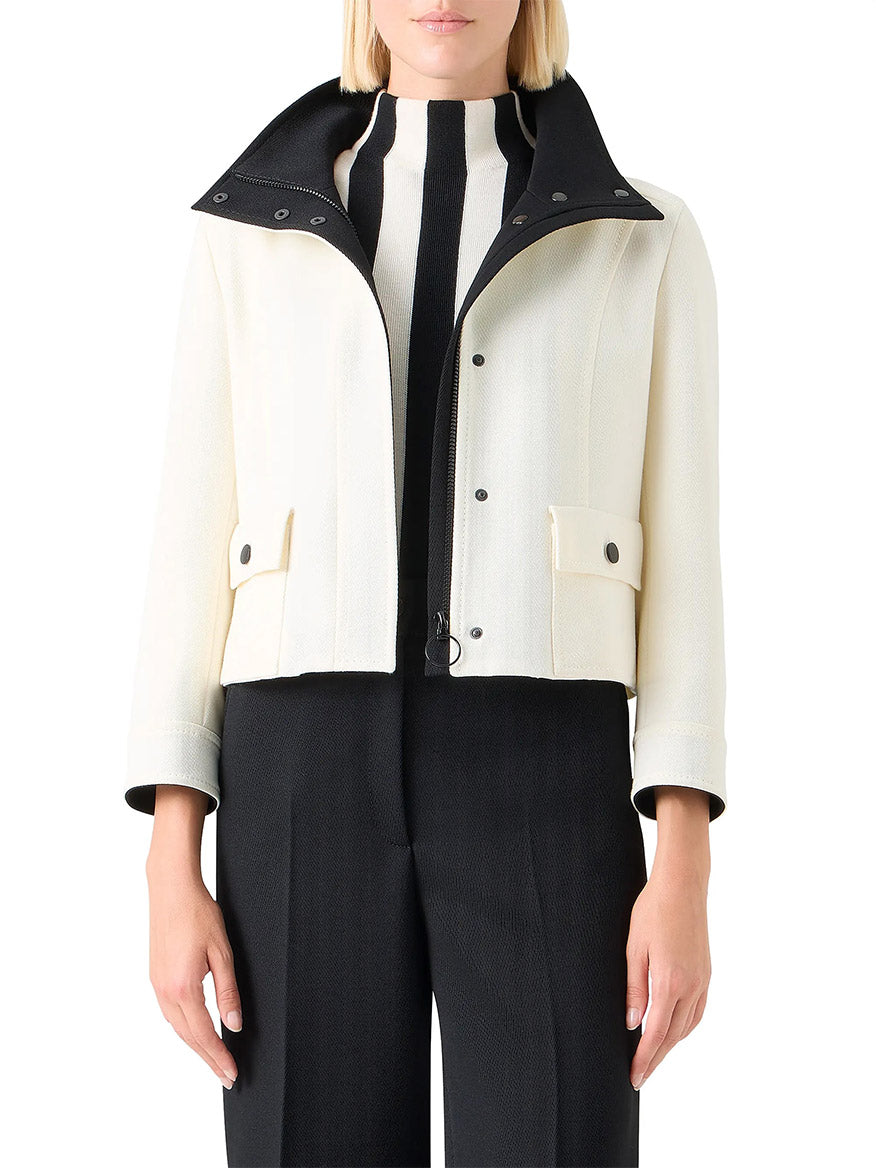 A woman wears the Akris Punto Wool Tricotine Stand Collar Jacket in Cream/Black with front buttons, layered over a black and white striped top and black pants.