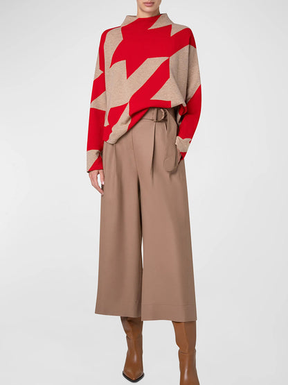 A person wearing an Akris Punto XL Houndstooth Wool/Cashmere Mockneck in Lipstick/Caramel, paired with beige wide-leg trousers and brown heeled boots, stands against a plain background.