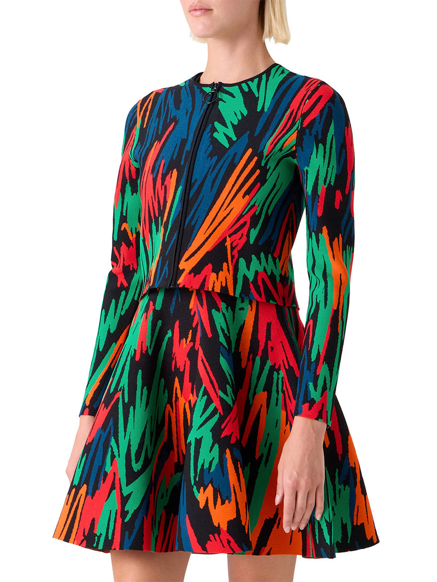 Someone wearing the Akris Punto Scribble Jacquard Cardigan in Black Multi, featuring long sleeves, a zip front, and a vibrant crayon-scribbled print in red, green, orange, and blue.