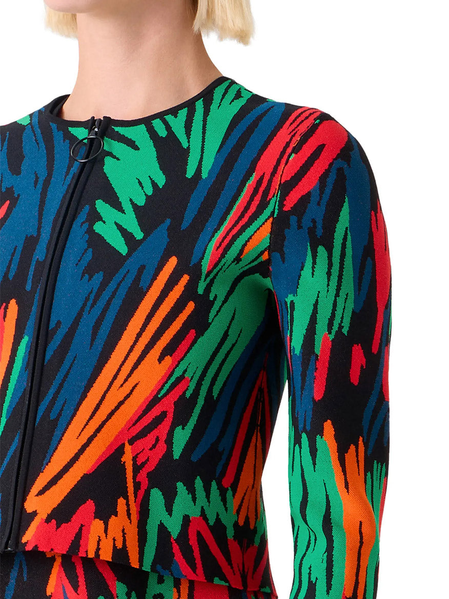 Close-up of a person wearing the Akris Punto Scribble Jacquard Cardigan in Black Multi, featuring bold multicolored abstract patterns reminiscent of crayon scribbles in orange, green, blue, and red.