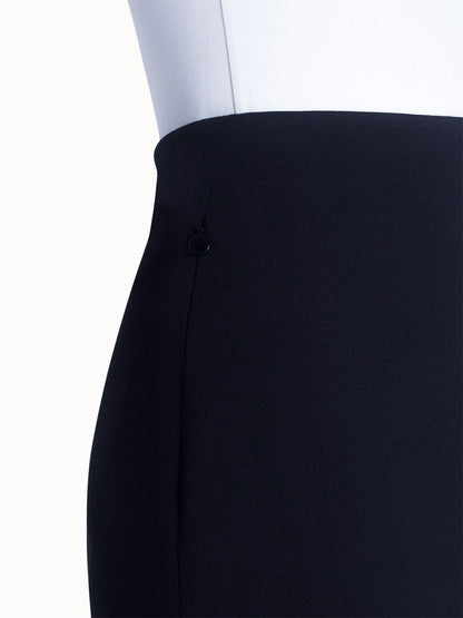 A close-up of a person in a white top tucked into the Akris Punto Jersey Stretch Skirt in Black, highlighting the high waist and left side seam with a small black ring detail.