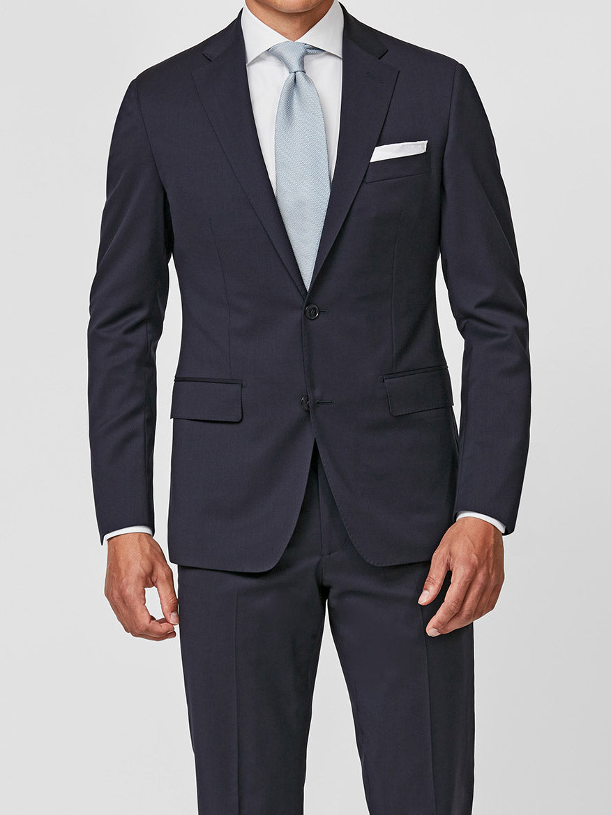 A man stands against a plain light background wearing the Atelier Munro Midnight Blue Twill 4-Season Wool Stretch Suit, paired with a light blue tie, white dress shirt, and white pocket square.