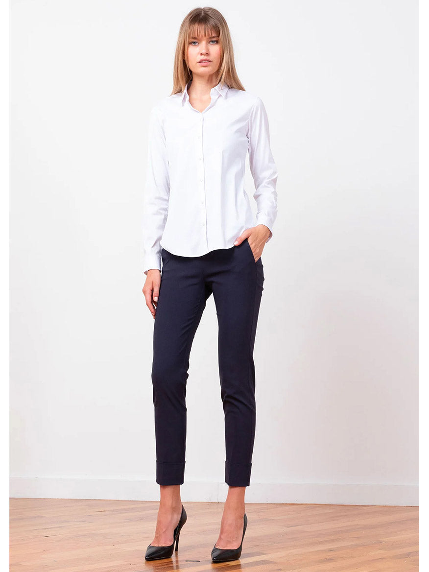 A person wearing a white button-up shirt, Avenue Montaigne Ben Signature Straight Leg Pant in Navy, and black heels stands against a plain white background on a wooden floor.