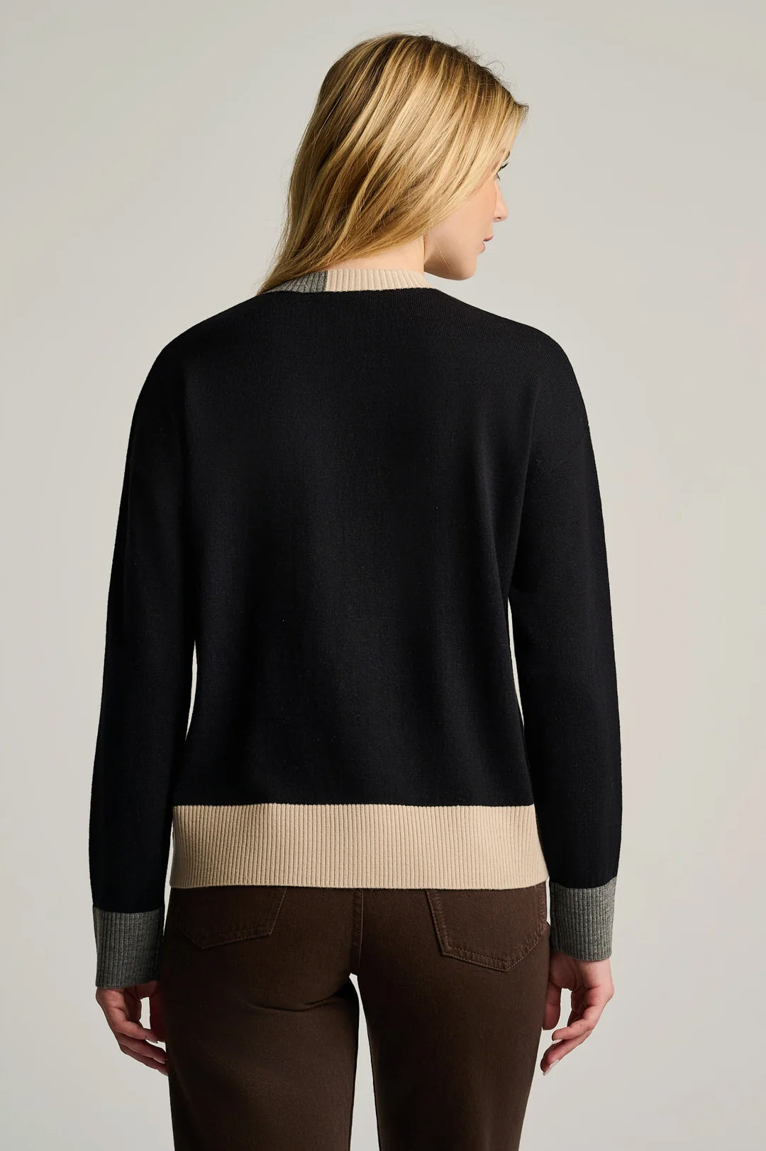 A blonde model showcases the Lisa Todd Bold Block Cotton Cashmere Sweater in Black, featuring a beige hem and cuffs, viewed from the back and paired with dark brown pants against a neutral background.