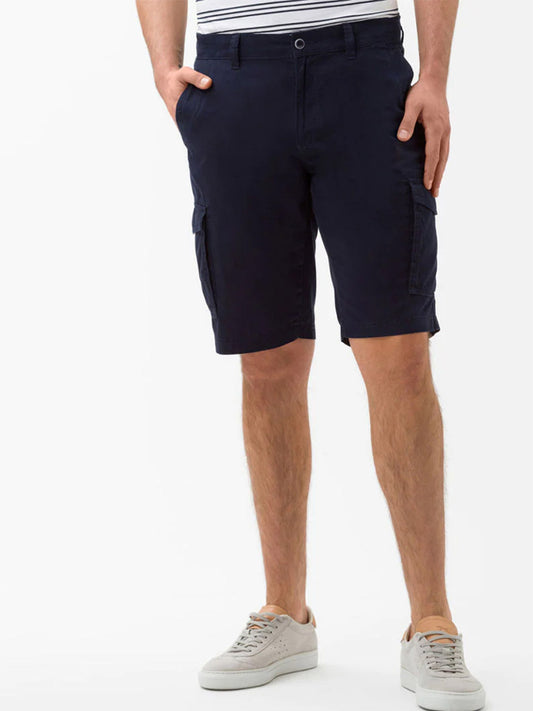 Man wearing Brax Brazil Cargo Shorts in Ocean and gray sneakers standing sideways.