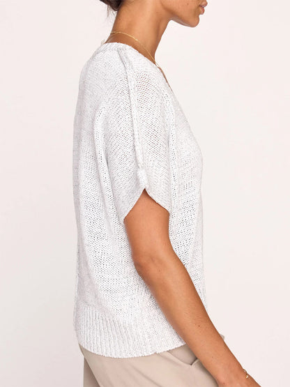 Side view of a woman wearing the Brochu Walker Gaia Tee in Glacier White, an elegant white knitted top with short sleeves and a unique shoulder cut-out, paired with light beige pants.