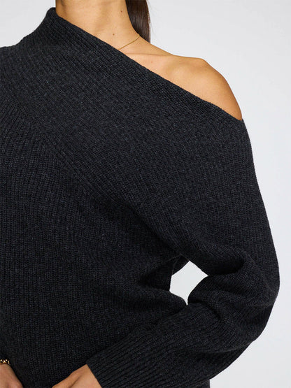 A person wears the Brochu Walker Hart Off-Shoulder Sweater in dark charcoal, made from soft Italian wool cashmere, revealing their left shoulder and part of their arm against a plain background.