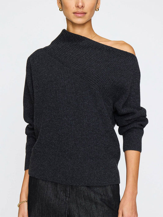 A person wears the Brochu Walker Hart Off-Shoulder Sweater in Dark Charcoal, crafted from Italian wool cashmere with rib stitch and long sleeves, paired with black pants against a plain background.