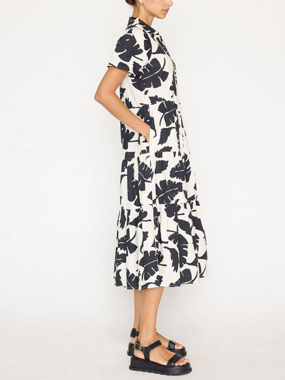 A woman stands profile wearing a knee-length, sleeveless black and white floral Brochu Walker Havana Dress in Tropical Combo and black platform sandals.