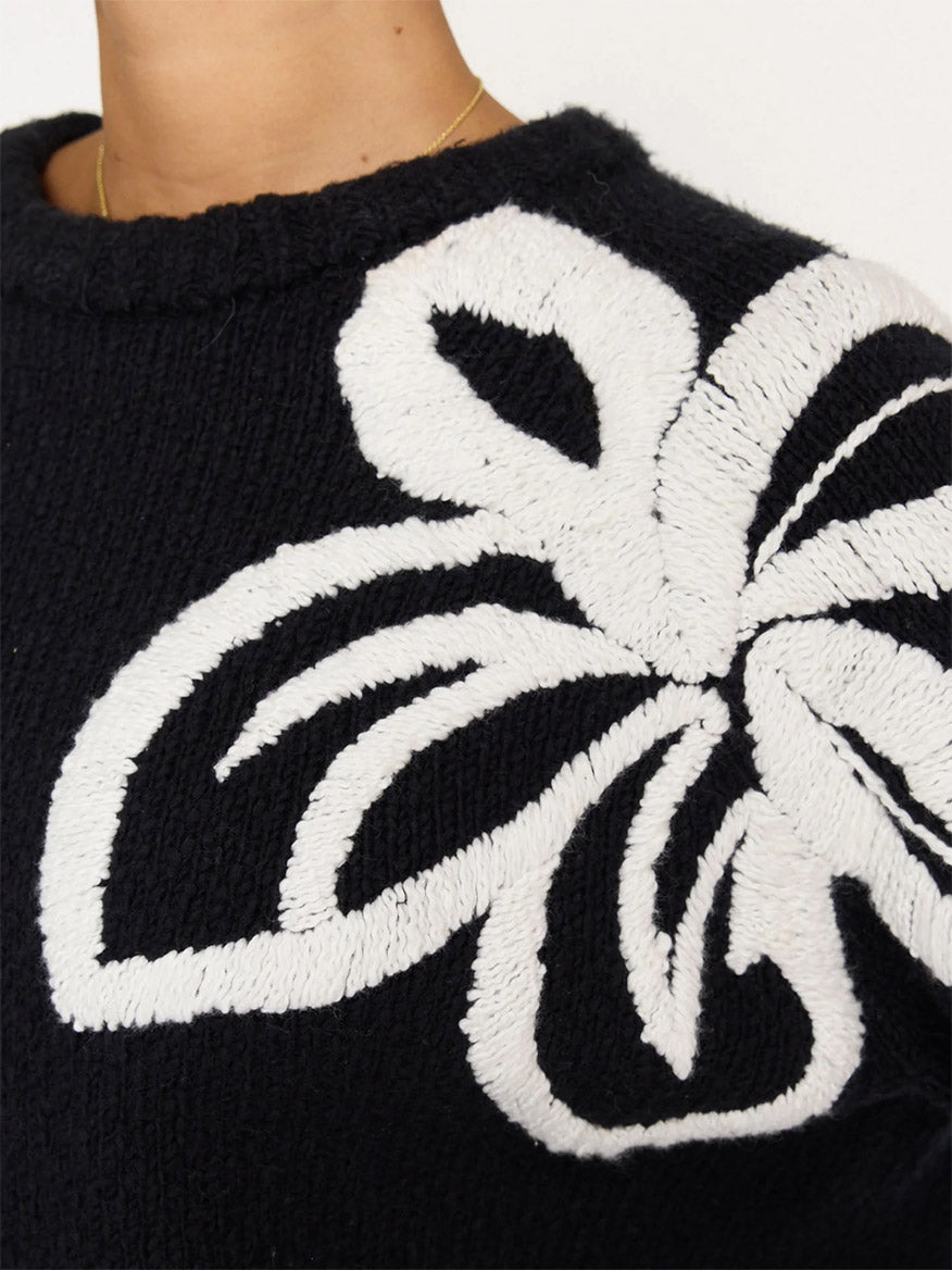 Close-up of a person wearing a black Brochu Walker Hibisicus Embroidered Sweater in Black Onyx with White featuring a large white floral design on the shoulder, made from soft organic cotton.