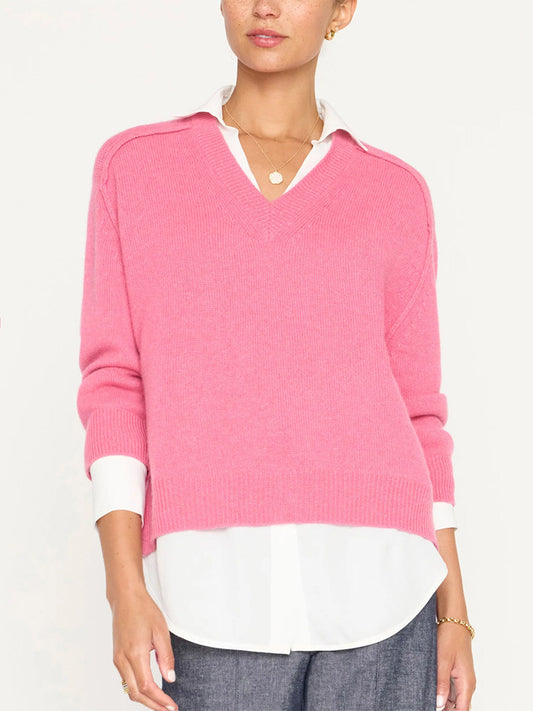A person wearing a pink, Brochu Walker Looker Layered V-Neck Pullover in Aster Pink over a white collared shirt, paired with gray pants and a gold necklace.