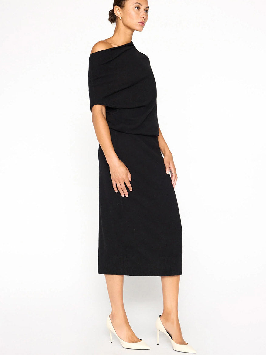 A person in a chic Brochu Walker Lori Sleeveless Dress in Black Onyx and white heels stands against a plain white background, with its versatile neckline adding elegance to the look.