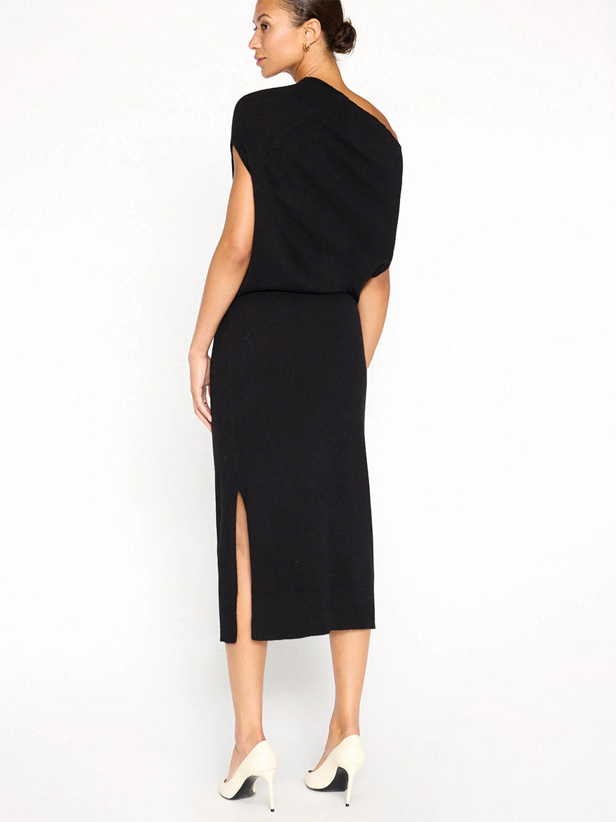 A woman stands wearing the Brochu Walker Lori Sleeveless Dress in Black Onyx, featuring a chic back slit, paired with white high heels, facing away.