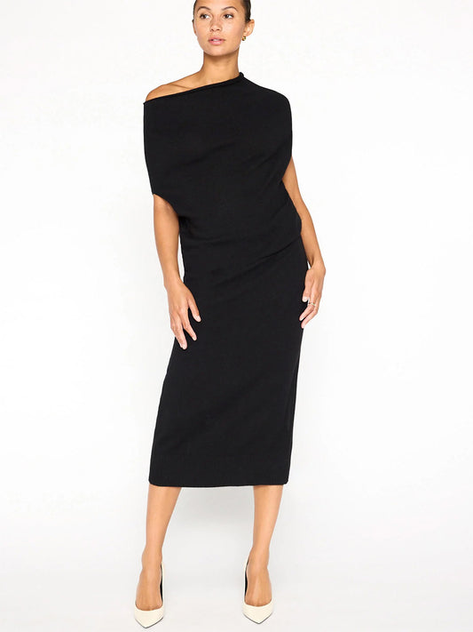 A person poses elegantly in the Brochu Walker Lori Sleeveless Dress in Black Onyx, showcasing its chic off-shoulder, versatile neckline. The mid-length attire pairs seamlessly with beige heels, set against a plain white background.