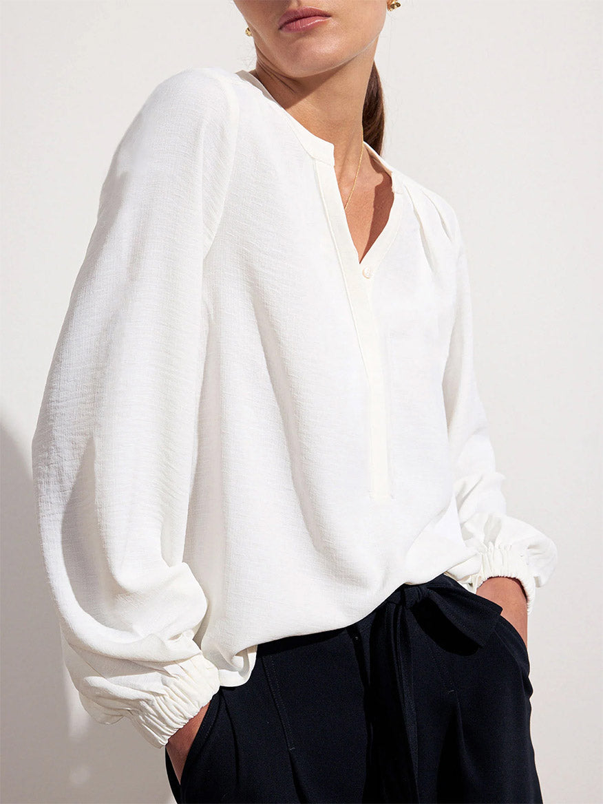 A person wearing the Brochu Walker Phoebe Blouse in Salt White, made from Italian creped fabric with long sleeves, paired with black pants, standing against a plain white background.