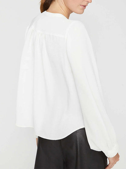 Dressed in the Brochu Walker Phoebe Blouse in Salt White, an elegant piece made from Italian creped fabric, the individual pairs it stylishly with black pants, presenting a graceful back view.