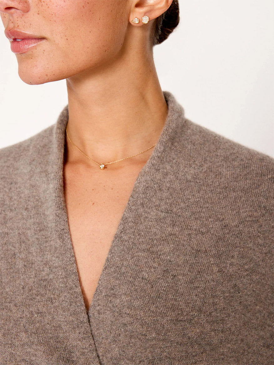 A close-up of a person wearing gold earrings and a simple gold necklace, with a grey **Brochu Walker Siena Wrap Neck Pullover in Otter Melange**, exuding an air of luxe femininity.