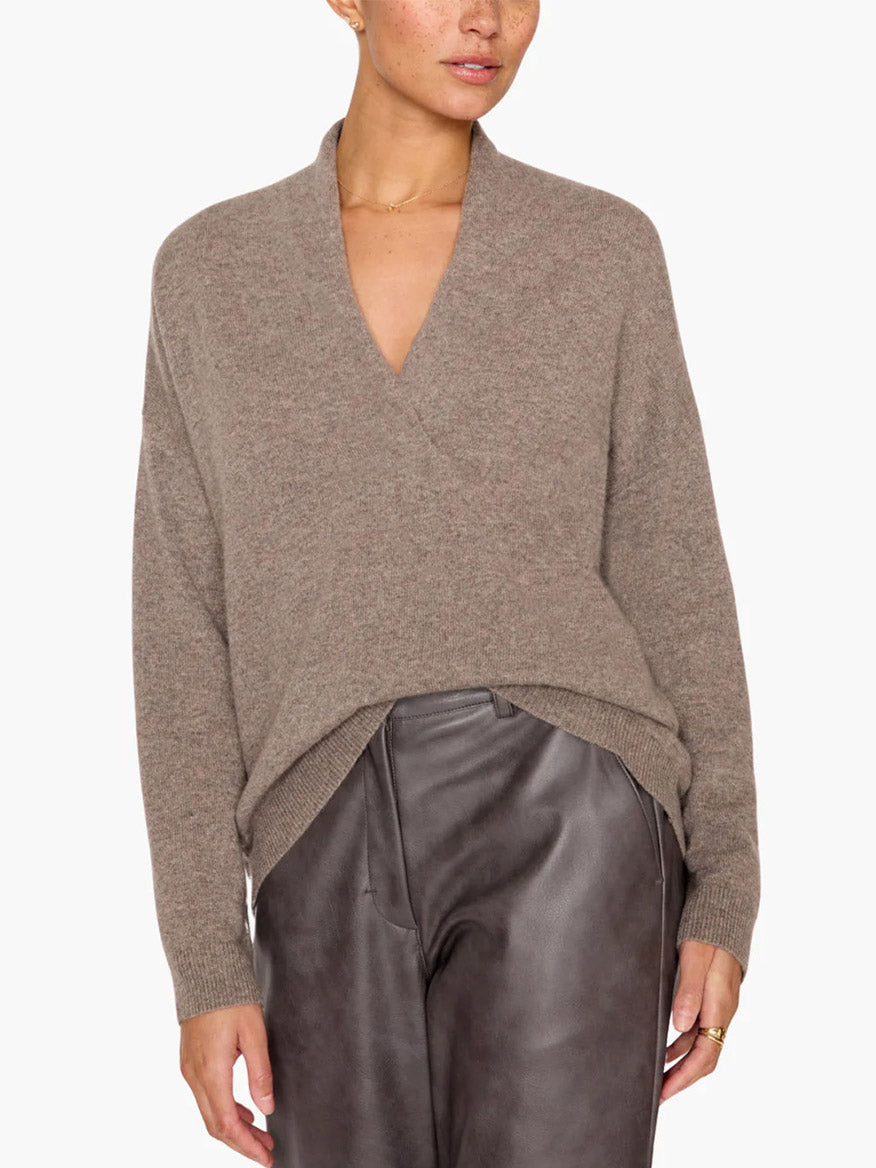 A person is wearing the Brochu Walker Siena Wrap Neck Pullover in Otter Melange and gray leather pants, standing against a plain background, exuding an air of luxe femininity.