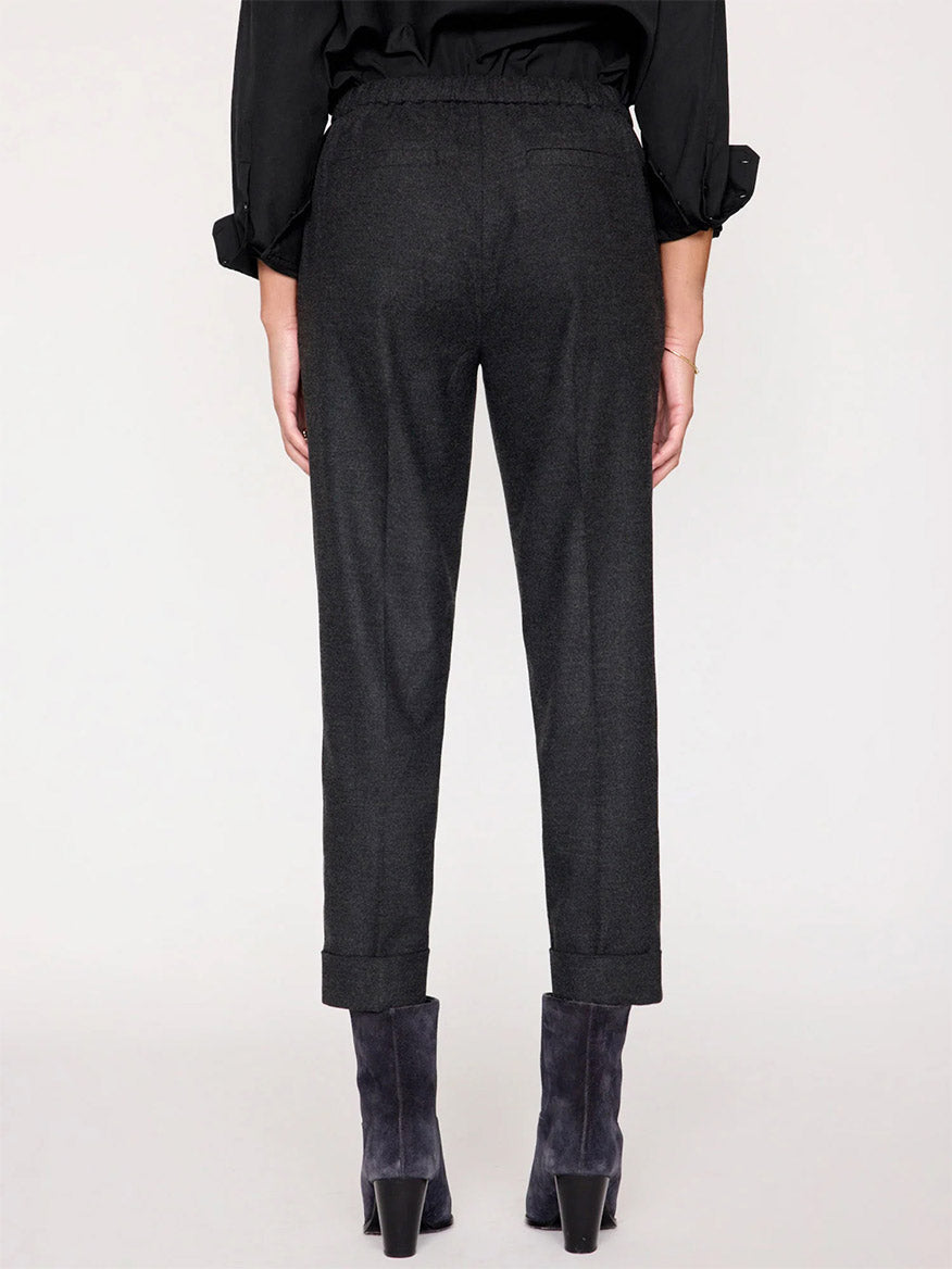 Rear view of a person wearing a black long-sleeve shirt, Brochu Walker Westport Brushed Pant in Dark Charcoal Melange with rolled cuffs, and gray suede ankle boots, standing against a plain background. These pants serve as a sophisticated everyday staple with their luxe feel.