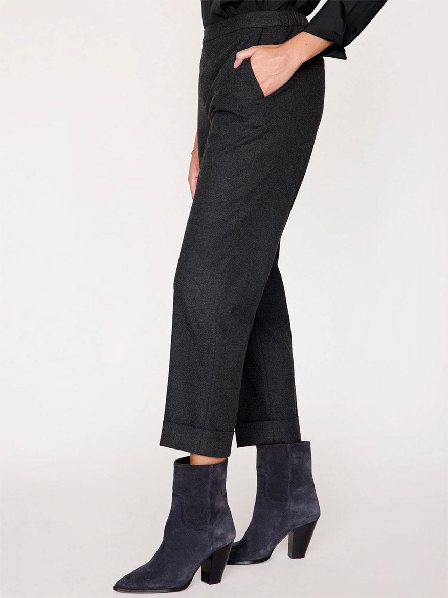 A person exudes a sophisticated everyday staple style, wearing dark cropped pants reminiscent of the Brochu Walker Westport Brushed Pant in Dark Charcoal Melange and suede ankle boots, standing confidently with one hand in their pocket.