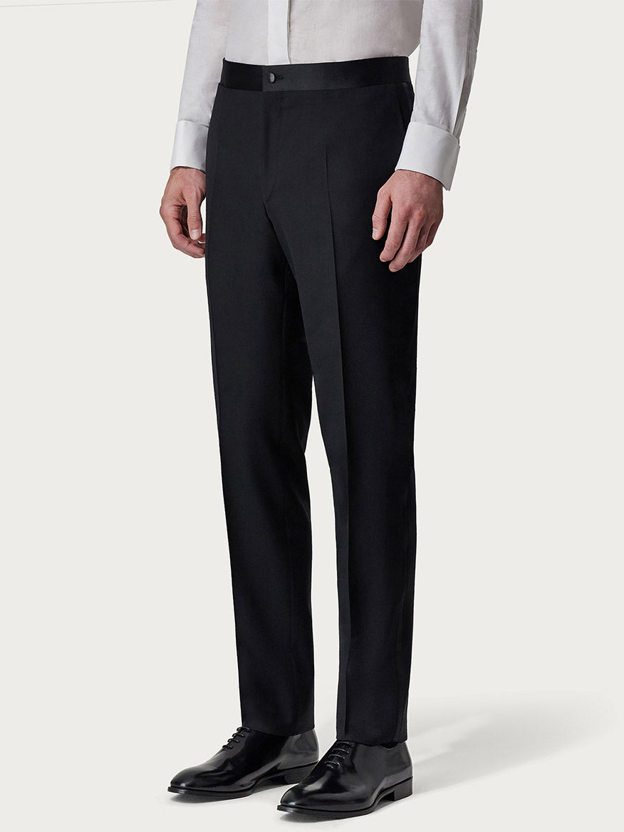Man in a Canali Siena Black Wool Tuxedo with peak lapels and black trousers standing against a light background, focusing on his lower half from the waist down.