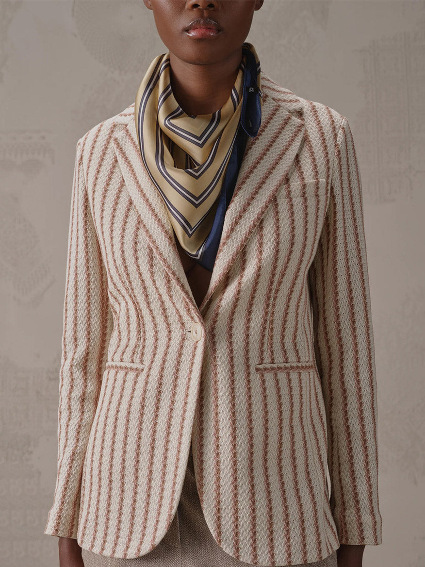 A person wearing the Circolo 1901 Slim Striped Long Jacket in Naturale Knitted, featuring beige and red stripes with a notch lapel and single button closure, layered over a beige top and a beige scarf with navy and white stripes.