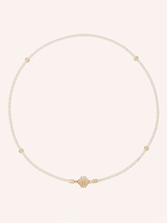 The Clara Williams Aspen Braided Leather Cream Mini Necklace features hand-crafted braided cream genuine leather with subtle gold accents and a central gold bead, finished with a 14K yellow gold clasp, displayed on a plain light background.