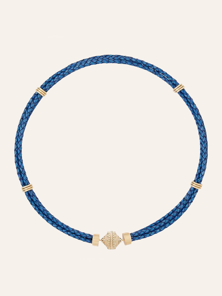 Clara Williams Aspen Braided Leather Denim Blue Necklace, crafted from braided denim blue genuine leather, features four 14K yellow gold bands and a central gold decorative bead, displayed against a plain light background.